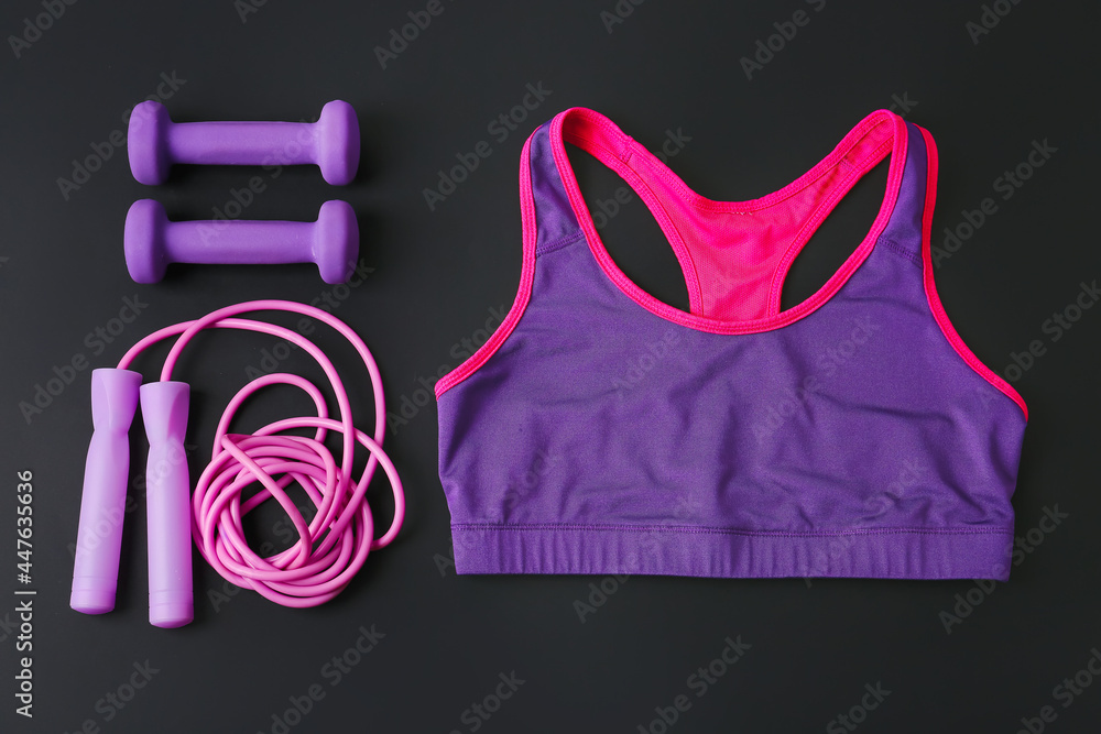 Sport top, skipping rope and dumbbells on dark background