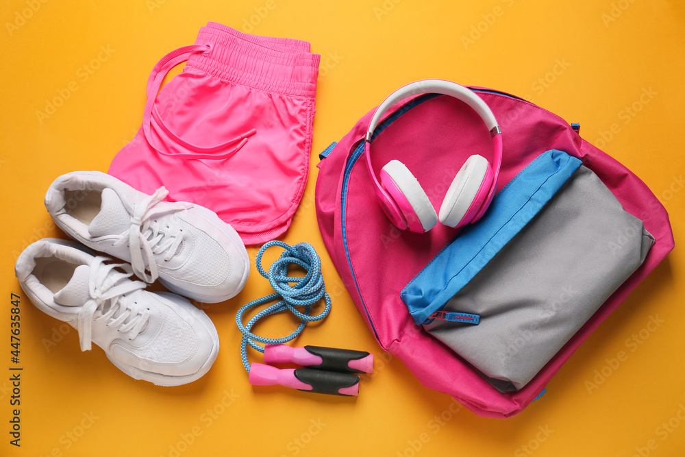 Sportswear, skipping rope, backpack and headphones on color background