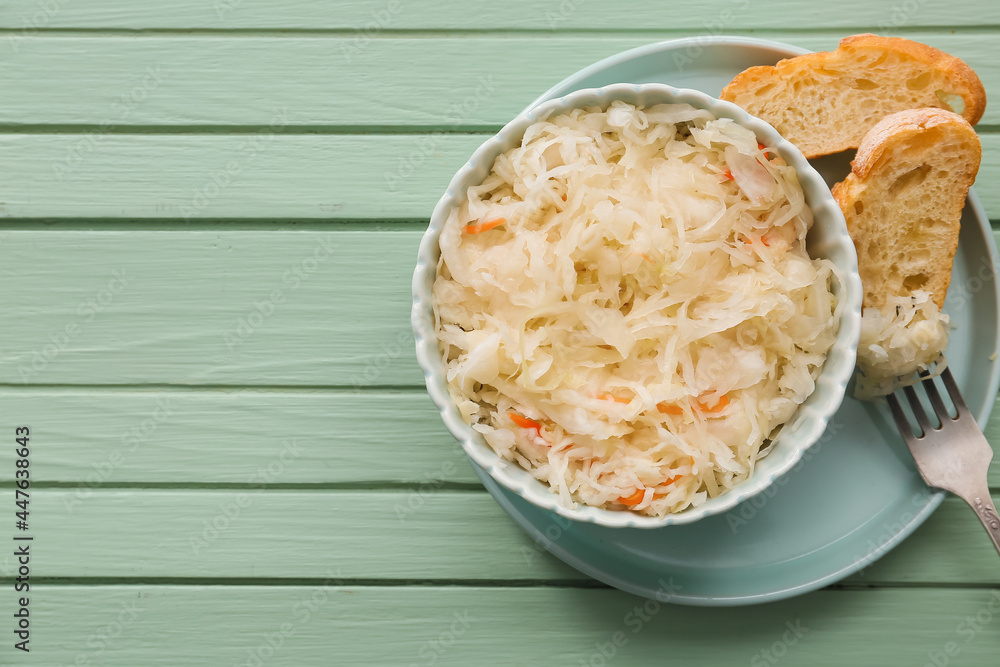 Bowl with tasty sauerkraut and fresh bread on color wooden background