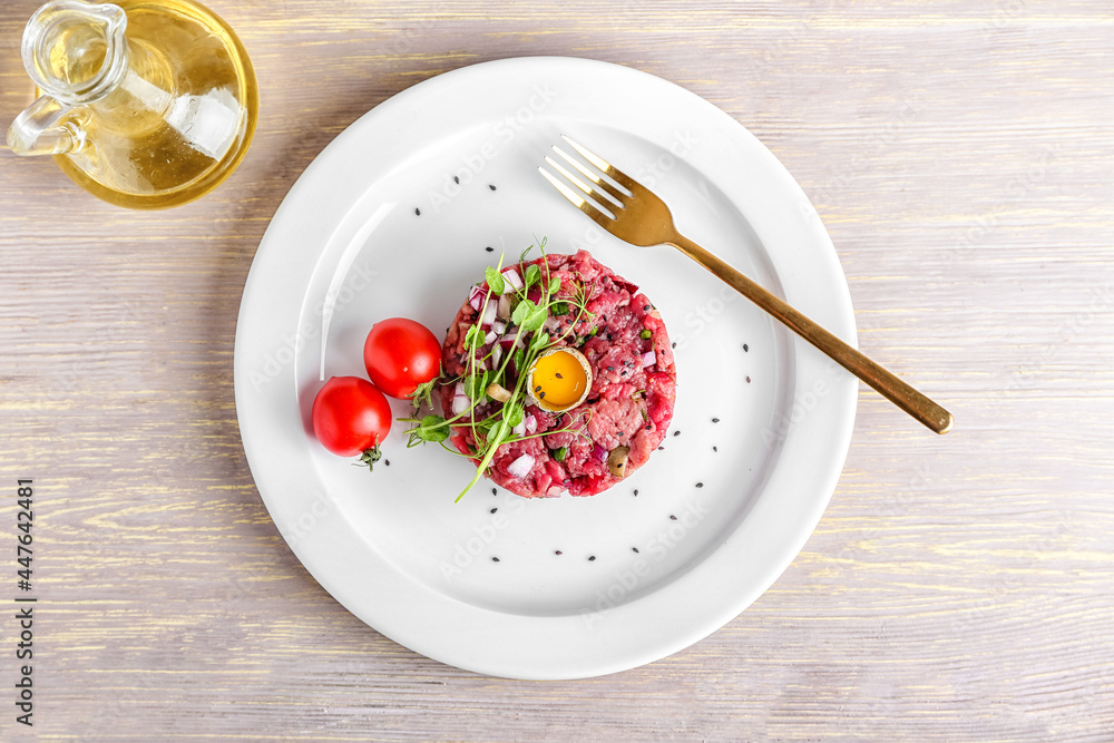 Plate with tasty beef tartare on light wooden background