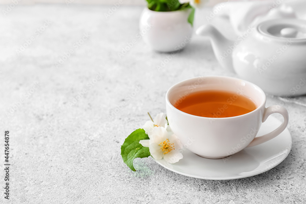 一杯茉莉花茶、茶壶和灯光背景下的花朵