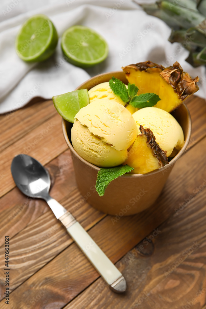 Paper bowl with tasty pineapple ice cream and lime on wooden background, closeup