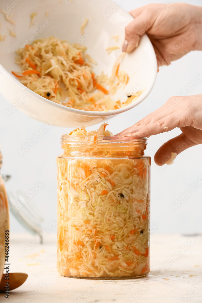 Woman putting tasty sauerkraut into glass jar on table in kitchen, closeup