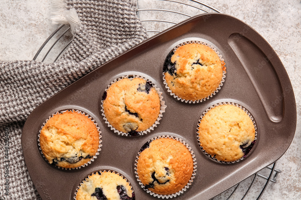 Baking tin with tasty blueberry muffins on light background, closeup