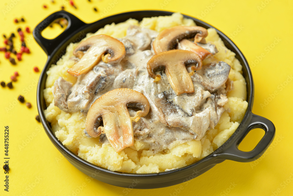 Frying pan with tasty mashed potatoes and mushrooms on color background