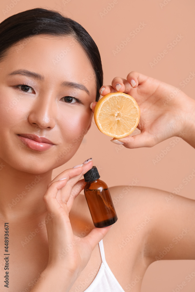 Beautiful young woman with lemon and bottle of essential oil on color background