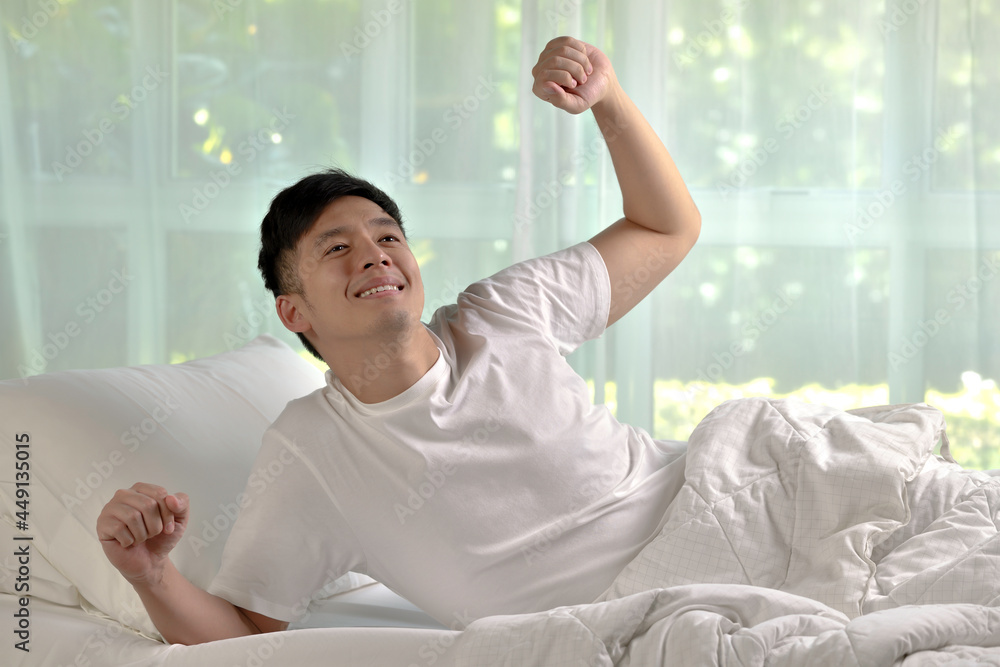 Asian man stretching in bed after wake up in the morning