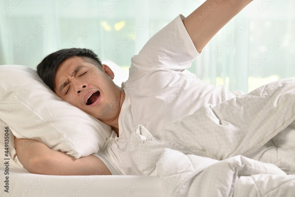 Young asian man yawning and stretching while waking up in the morning