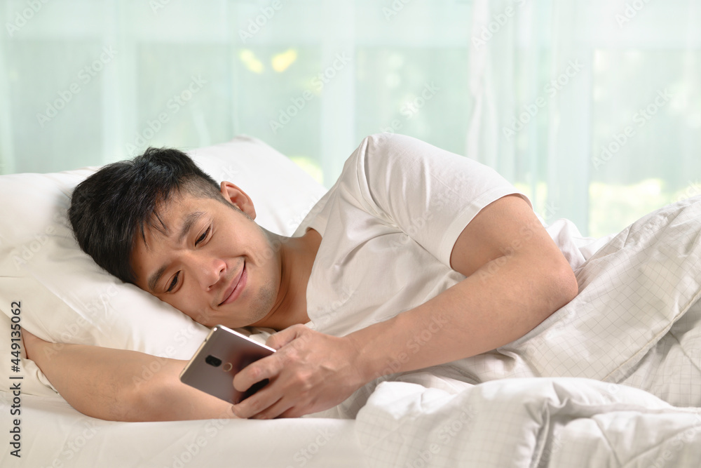 Young Asian man using smartphone in bed after waking up in the morning..