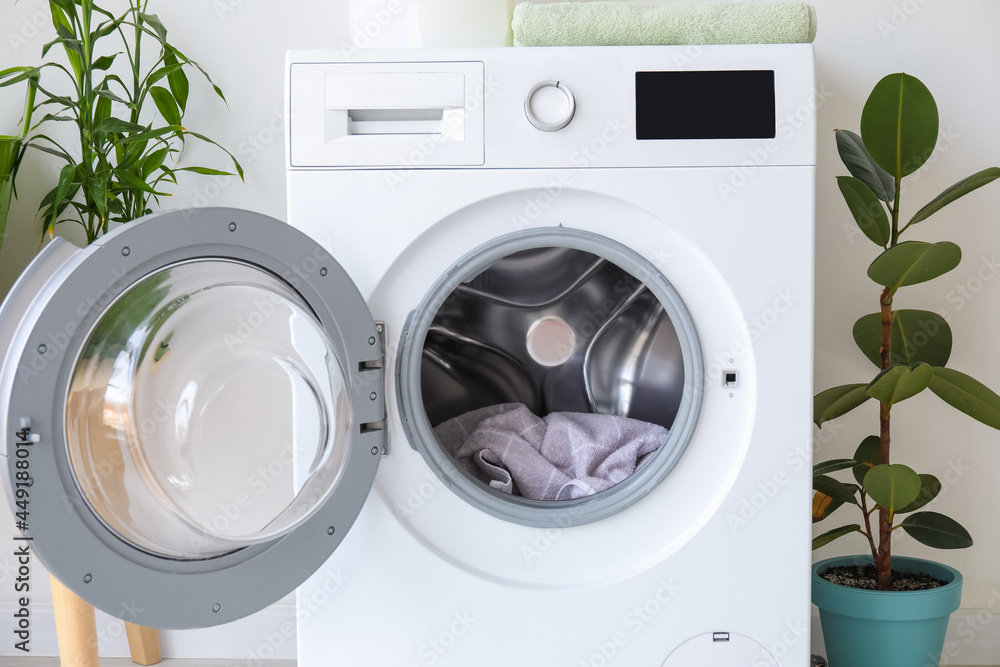 Modern washing machine with laundry near light wall