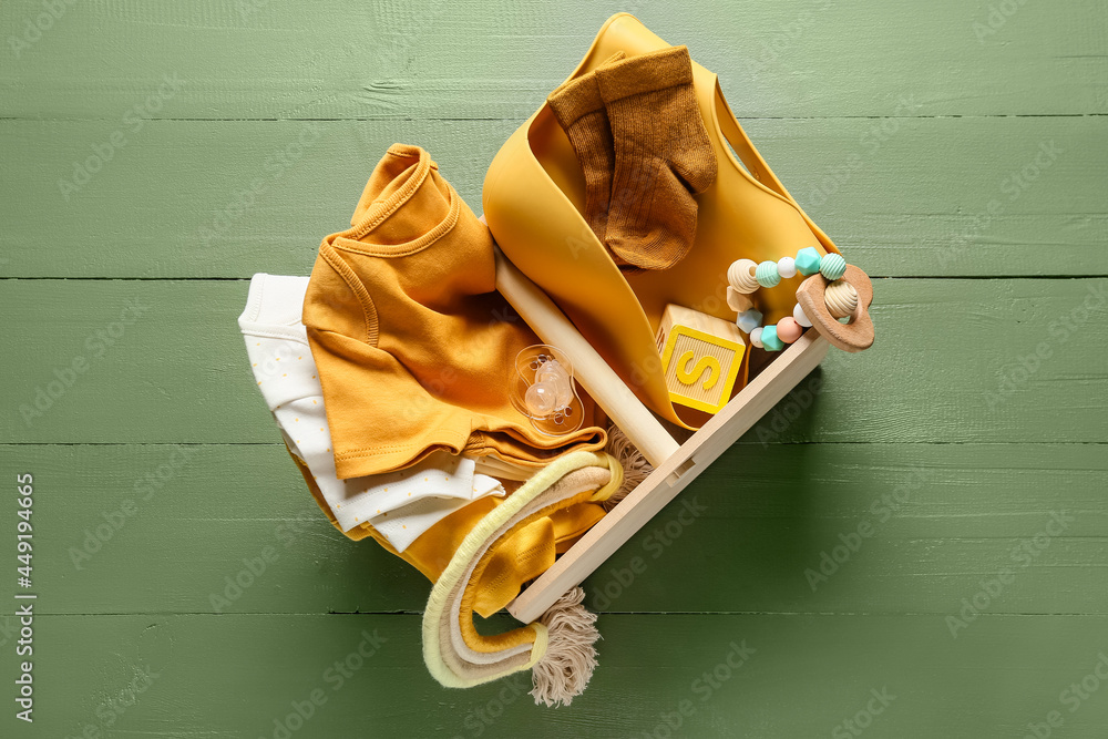 Basket with baby clothes, toys and accessories on color wooden background