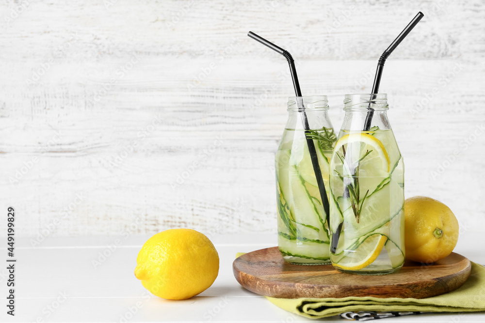 Bottles with cucumber lemonade on light wooden background