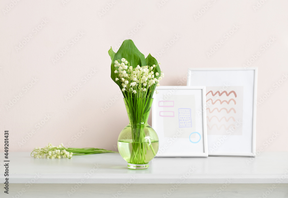 Vase with lily-of-the-valley flowers and pictures on shelf