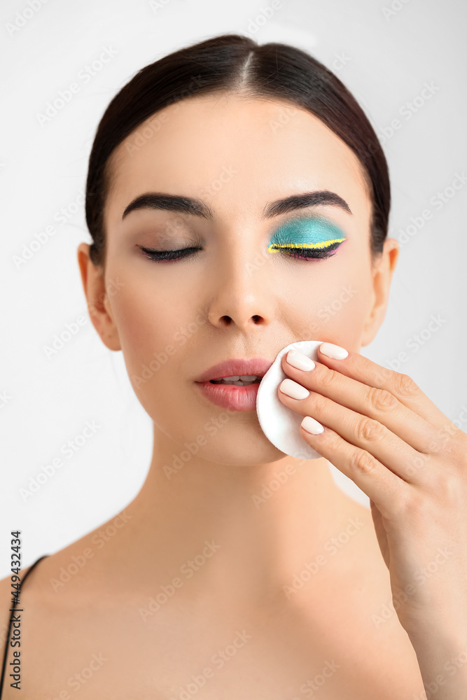 Beautiful young woman removing makeup on light background