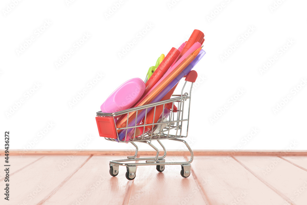 Shopping cart with stationery on wooden table against white background