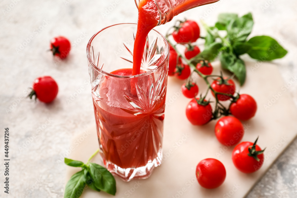 Pouring of tasty tomato juice in glass on light background