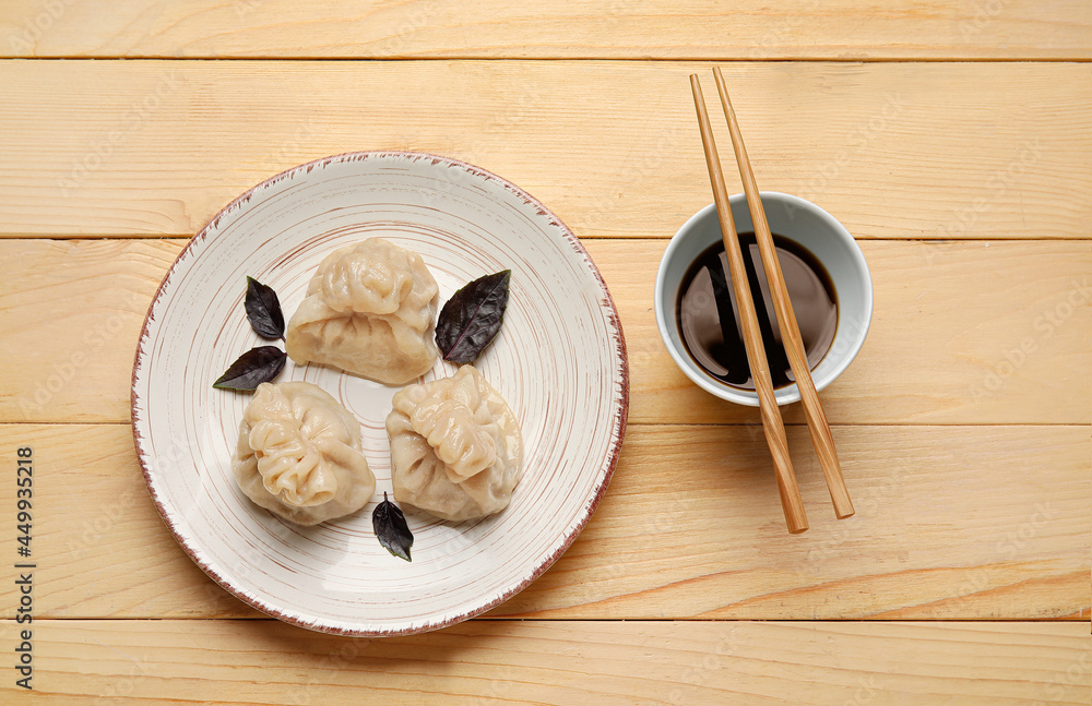 木制背景上有美味的饺子、筷子和一碗酱汁的盘子