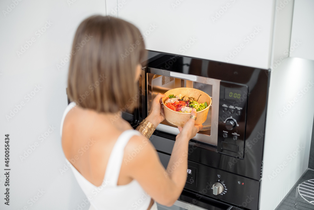 女性在家用微波炉加热食物，女性使用现代厨房电器