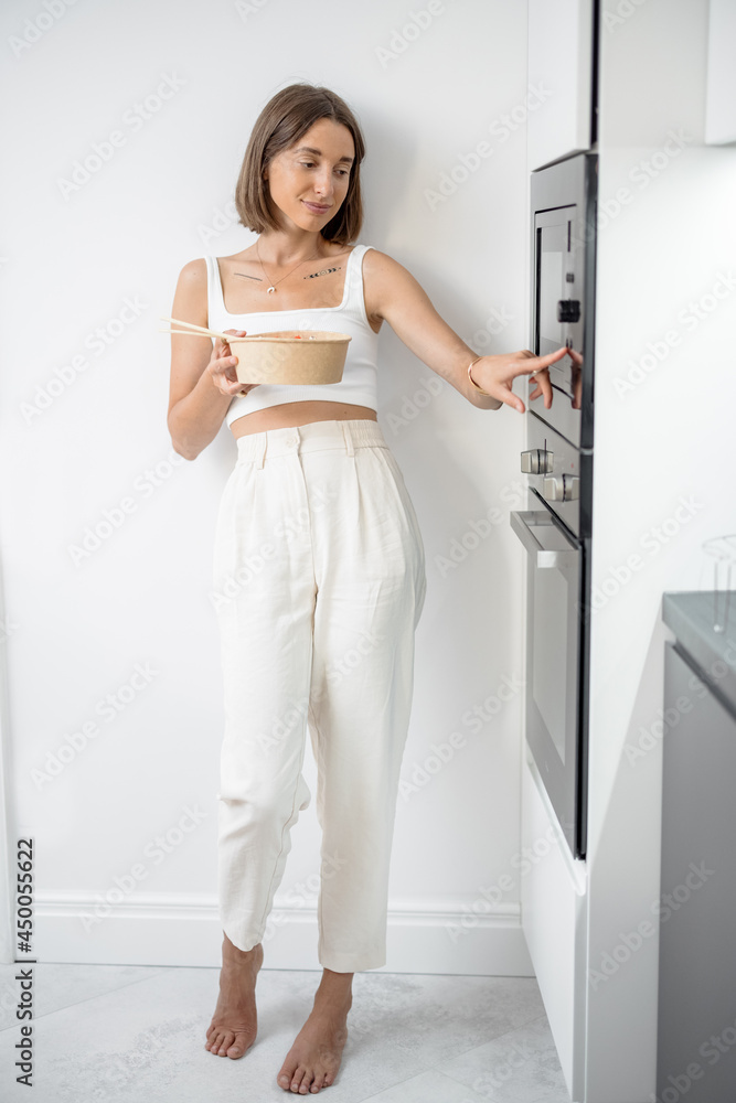 Happy woman eating asian takeaway food heated in microwave machine at home. Concept of modern and he