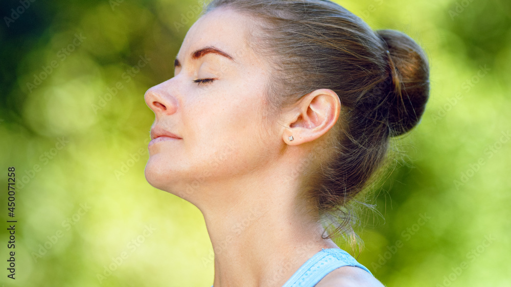 Blonde woman in blue top practices breathing exercises sitting in yoga pose under sunlight