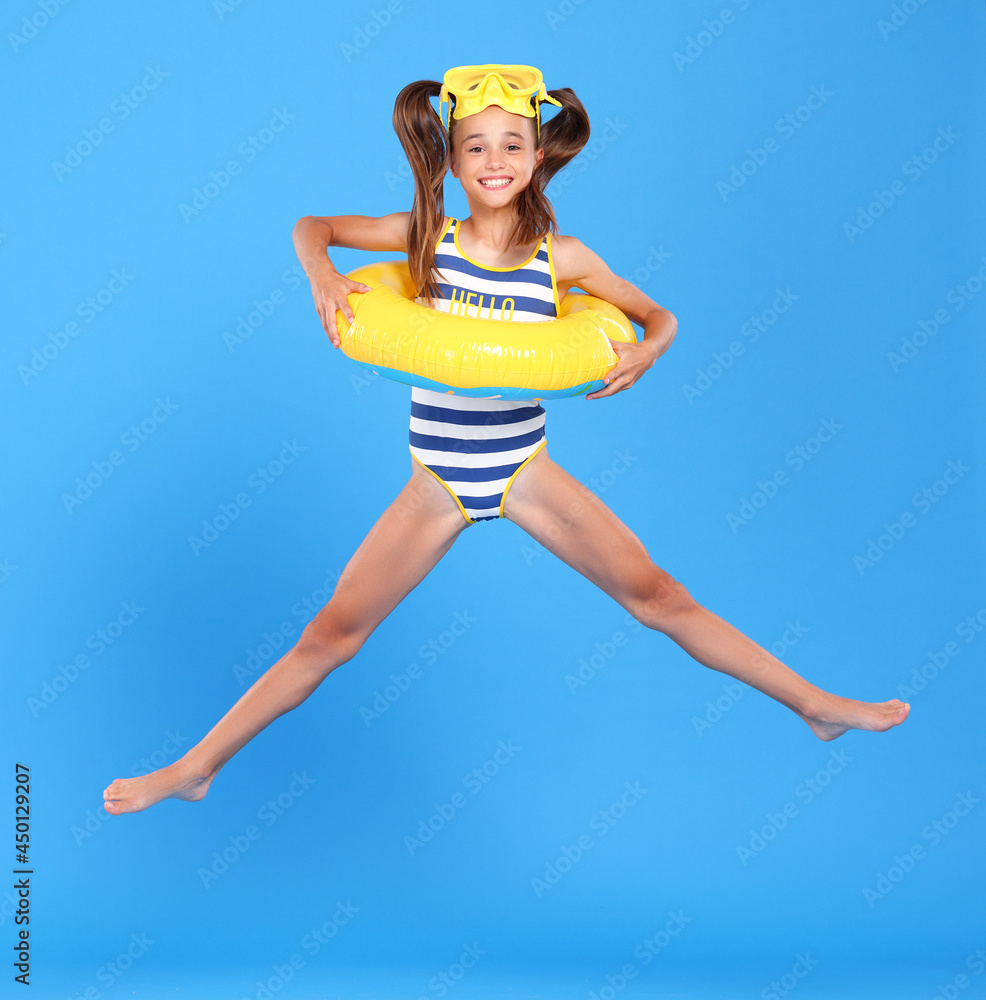 Little funny happy girl in swimsuit and goggles on her head jumping up in air with inflatable ring