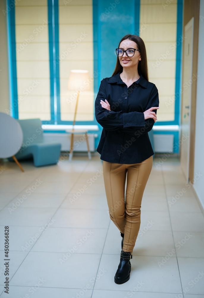 Full length view of the attractive woman in dark shirt and glasses standing arms crossed in hall and