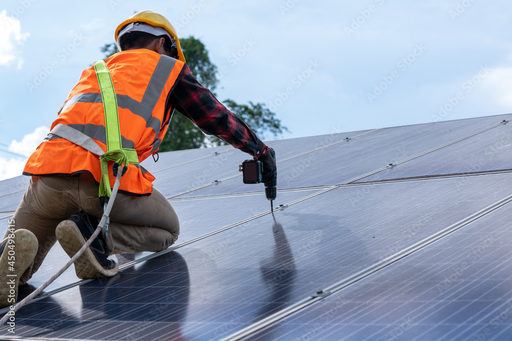 Solar panel technician with drill installing solar panels on roof at solar panel field,Environmental