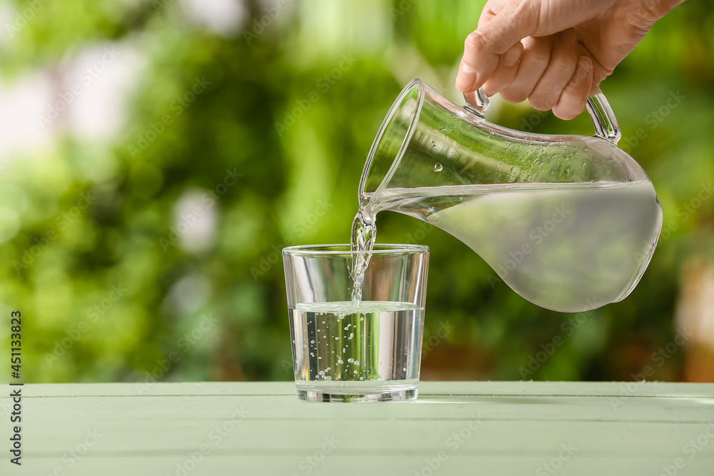 Woman pouring fresh water from jug into glass on table outdoors, closeup