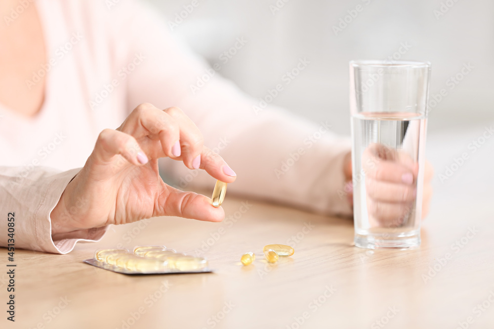 Mature woman taking fish oil at home, closeup