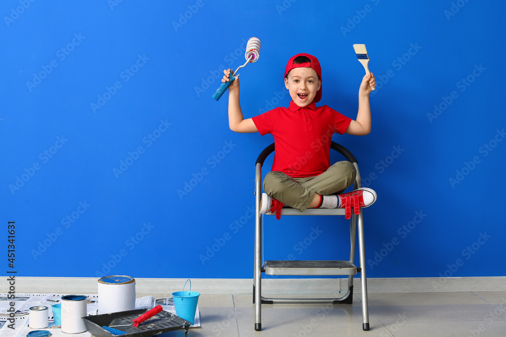 Little painter with roller and brush near color wall