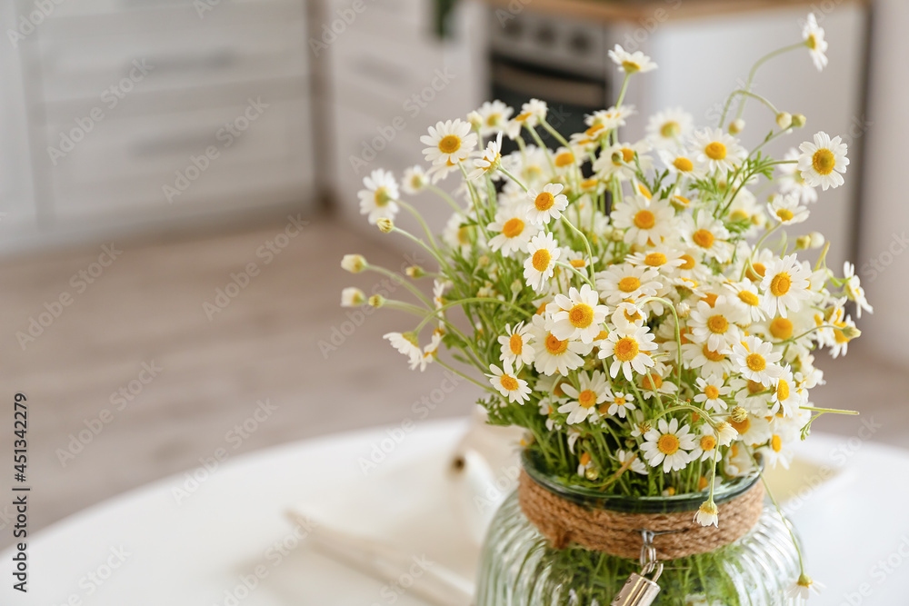 Vase with chamomiles on table in kitchen, closeup