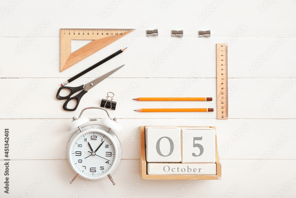 Cube calendar, alarm clock and stationery on white wooden background