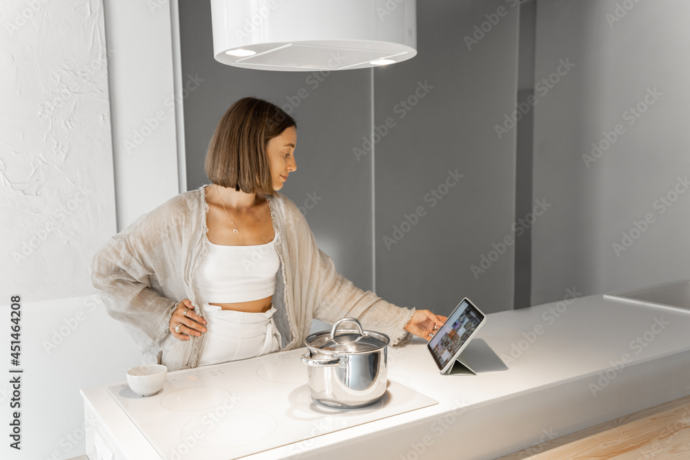 Woman using a digital tablet, looking on recipes while cooking at modern kitchen