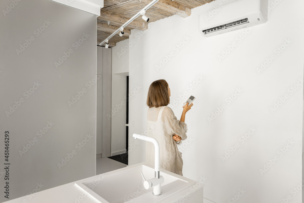 Woman sets the temperature on the air conditioner with remote control, while standing at modern whit