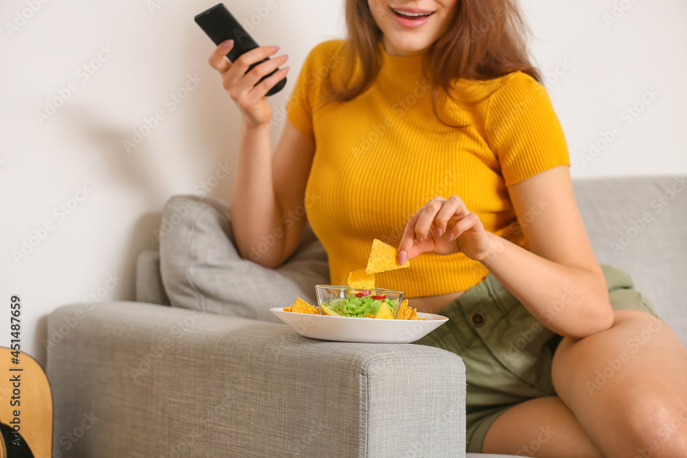 美丽的年轻女子在家看电视时吃着美味的玉米片