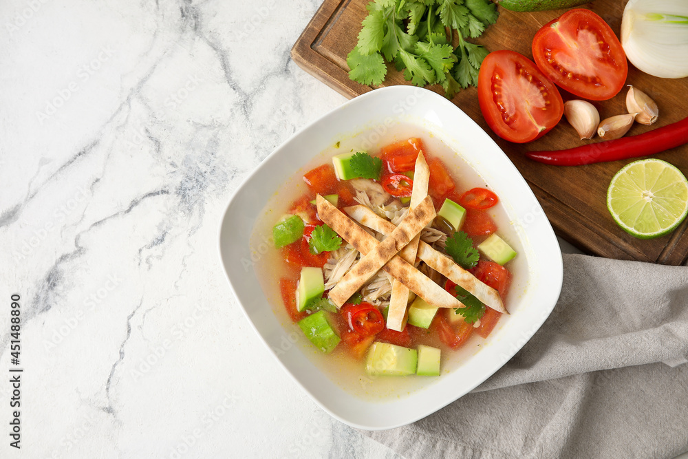 Bowl of tasty Sopa de Lima soup and ingredients on light background