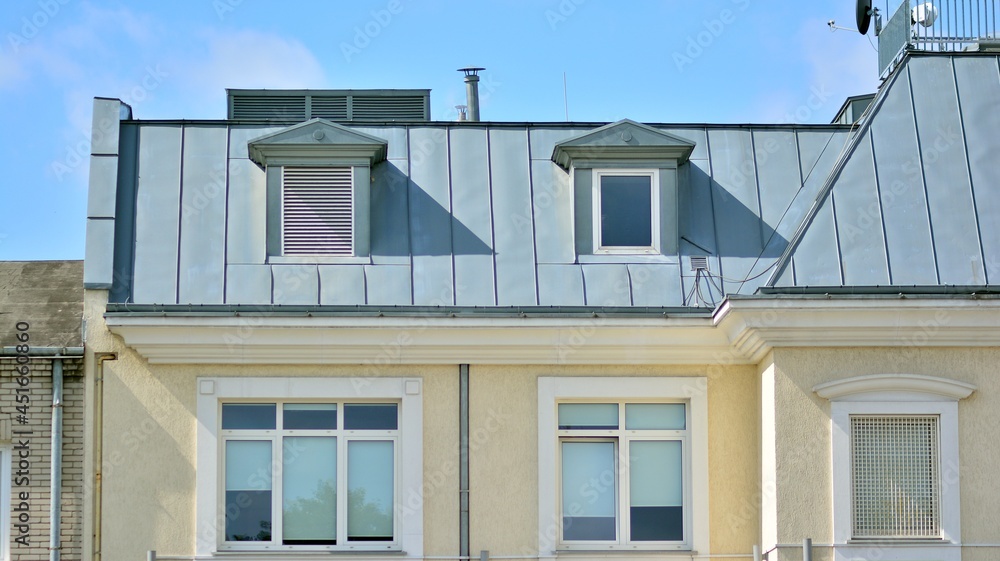 A gray metal roof in a stylish building. with wooden shutters and apartments in the attic with metal