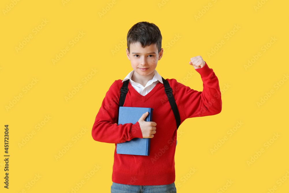 Little schoolboy with book on color background