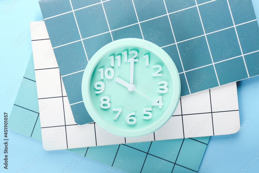 Stylish alarm clock and notebooks on color background, closeup