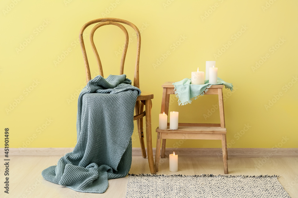 Knitted plaid on chair and table with candles near color wall