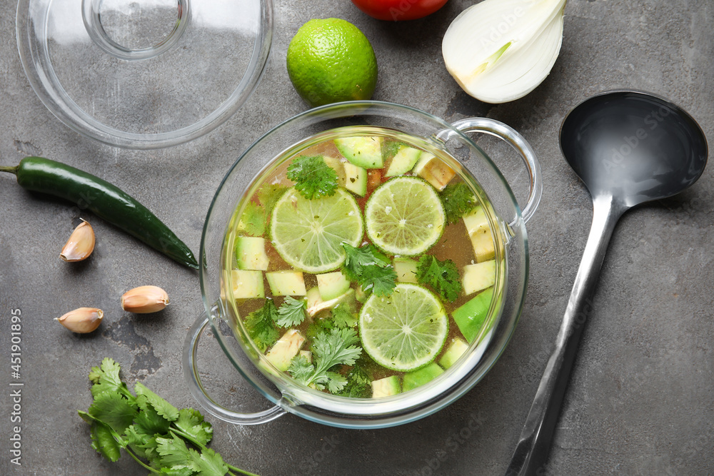 Pot with tasty Sopa de Lima soup and ingredients on dark background