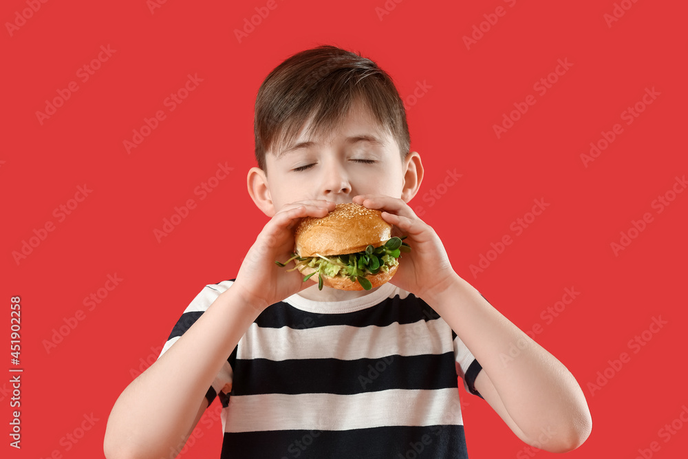 Little boy eating tasty vegan burger on color background