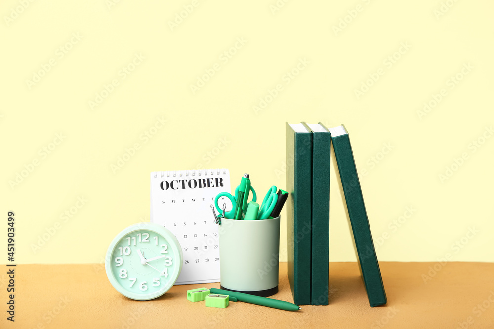 Flip calendar with alarm clock and stationery on table near color wall