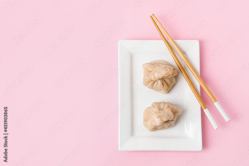 Plate with tasty dumplings and chopsticks on color background