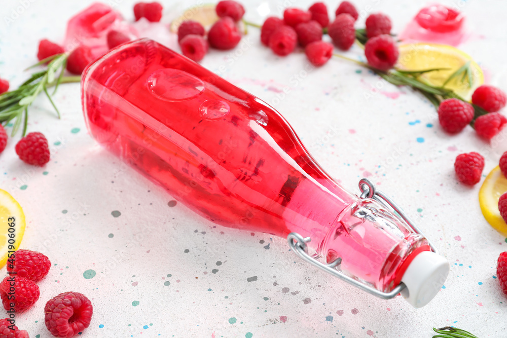 Bottle of tasty raspberry lemonade and berries on light background, closeup