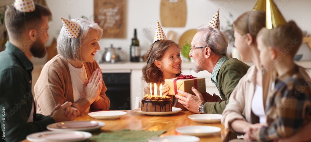 Loving senior  man giving gift to excited happy granddaughter during Birthday celebration with famil