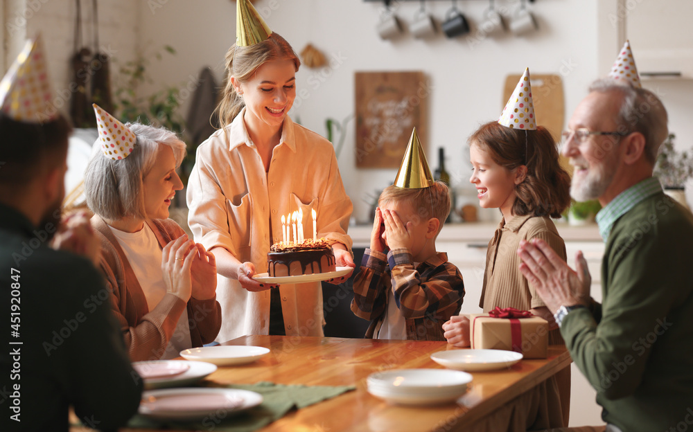 Happy big family surprising excited little boy by bringing Birthday chocolate cake with lit candles