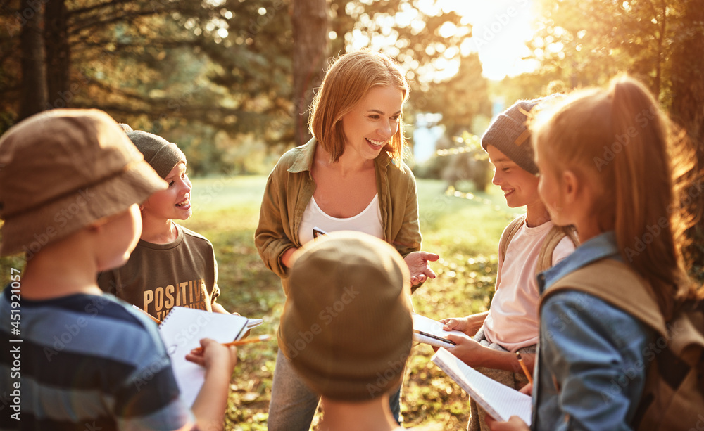 Positive female teacher interacting with school kids boys and girls during ecology lesson in forest