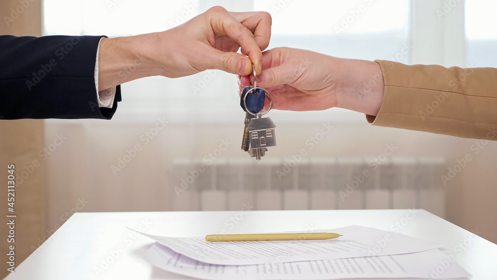 Realtor shakes hand and gives keys to female client above table with signed apartment rental agreeme