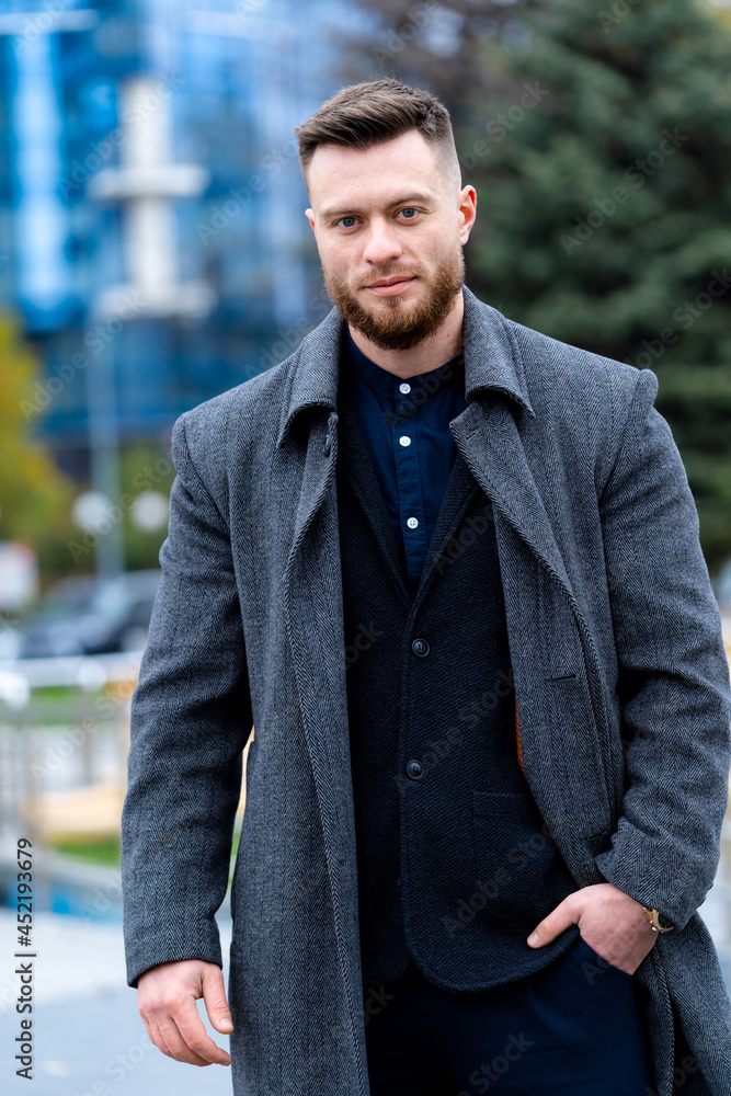 Stylish man holding hand on coat and walking near high buildings. Man relaxing walk on modern street